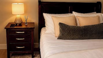 A neatly made bed with white linens and a dark wooden headboard, a bedside table with a lamp and a phone, and a framed artwork on the wall.