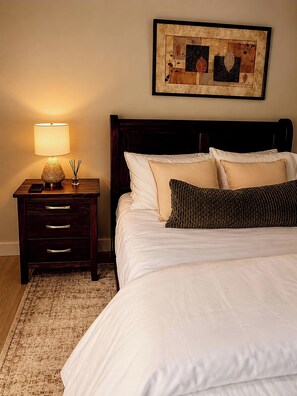 A neatly made bed with white linens and a dark wooden headboard, a bedside table with a lamp and a phone, and a framed artwork on the wall. - Charming 1-bedroom Suite With Ocean View in Prince Rupert (Prince Rupert)