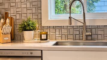A modern kitchen with a built-in dishwasher, a stainless steel sink, and a window with a view of trees.
