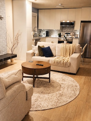A modern living room with a sofa, coffee table, and a kitchen in the background. - Charming 1-bedroom Suite With Ocean View in Prince Rupert (Prince Rupert)