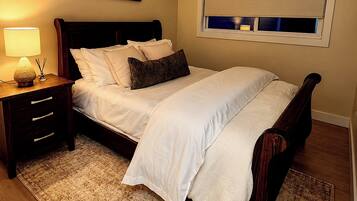 Un dormitorio con cama, mesitas de noche, un ventanal con persianas y un cuadro colgado en la pared.
