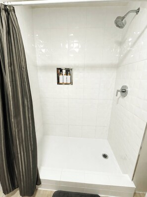 Zona de ducha con alcachofa, desagüe y panel de control con botellas.