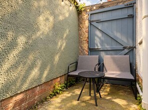 A small outdoor seating area with a table and two chairs, a textured wall, and a blue gate. - Stylish Home In Hartlepool, Free Parking & Wifi (Hartlepool)