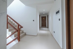 Un couloir avec un escalier en bois sur la gauche, une porte au fond et un interrupteur sur le mur.