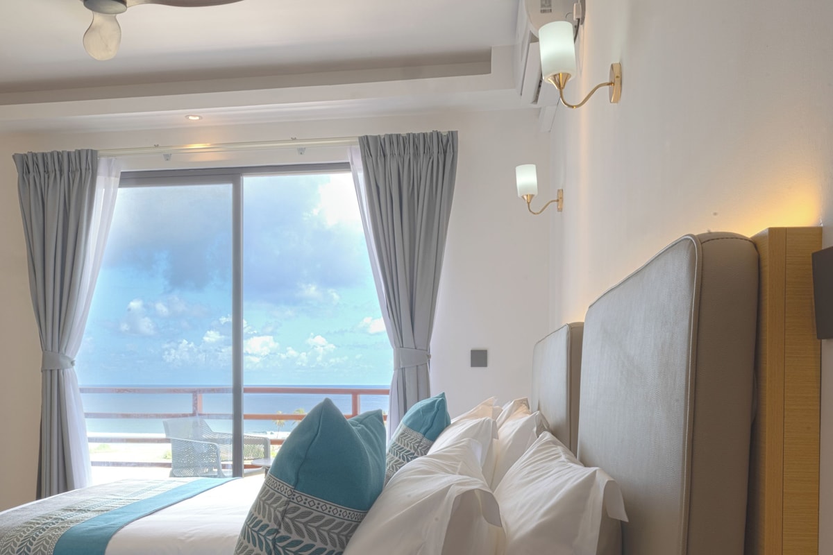Une chambre d’hôtel avec un grand lit, deux oreillers, une tête de lit et une vue sur la mer.