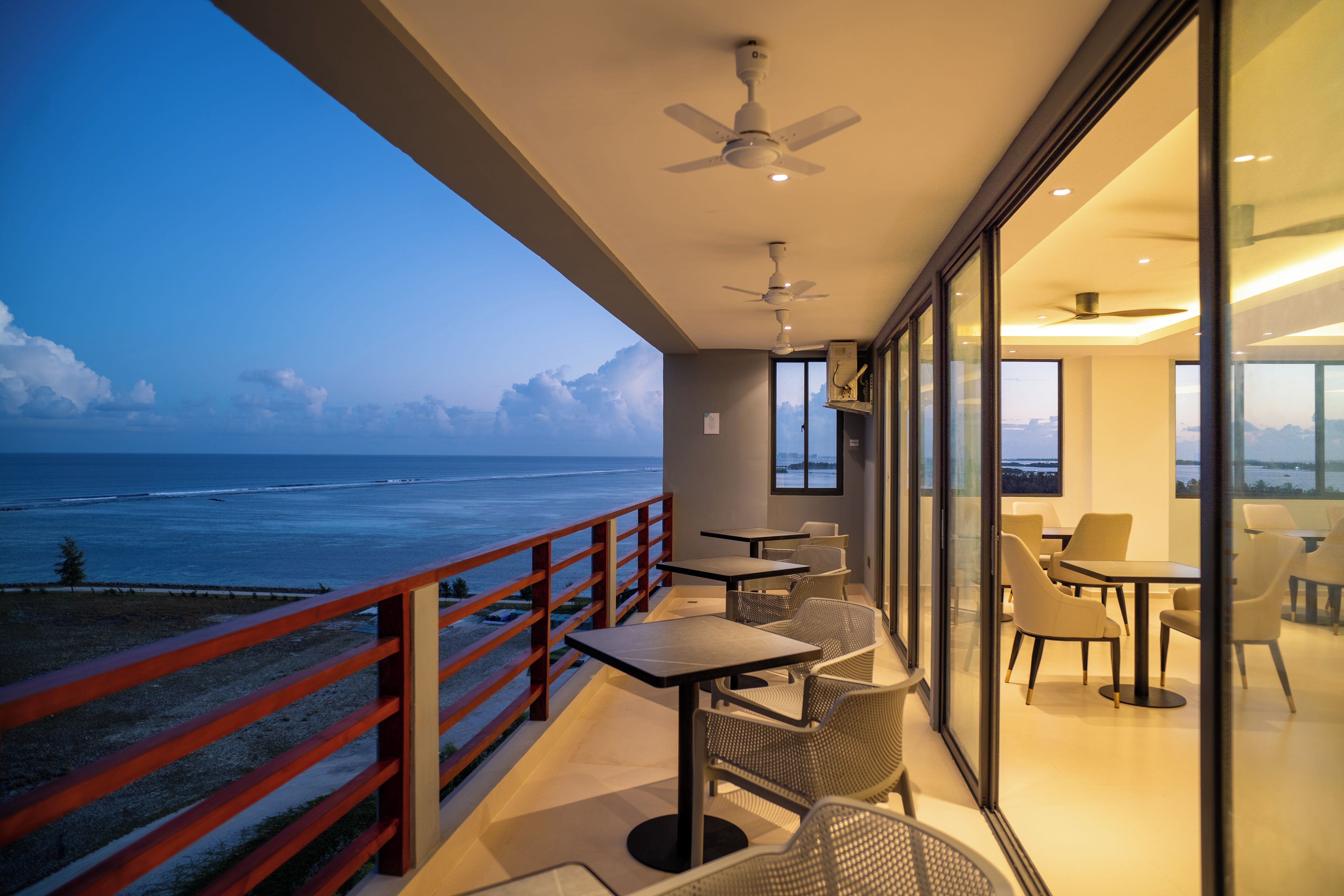 A balcony with a view of the ocean, equipped with tables and chairs.