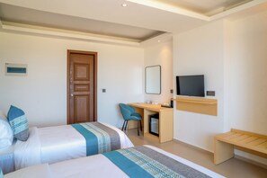 A hotel room with two beds, a desk, a chair, a television, and a bench.
