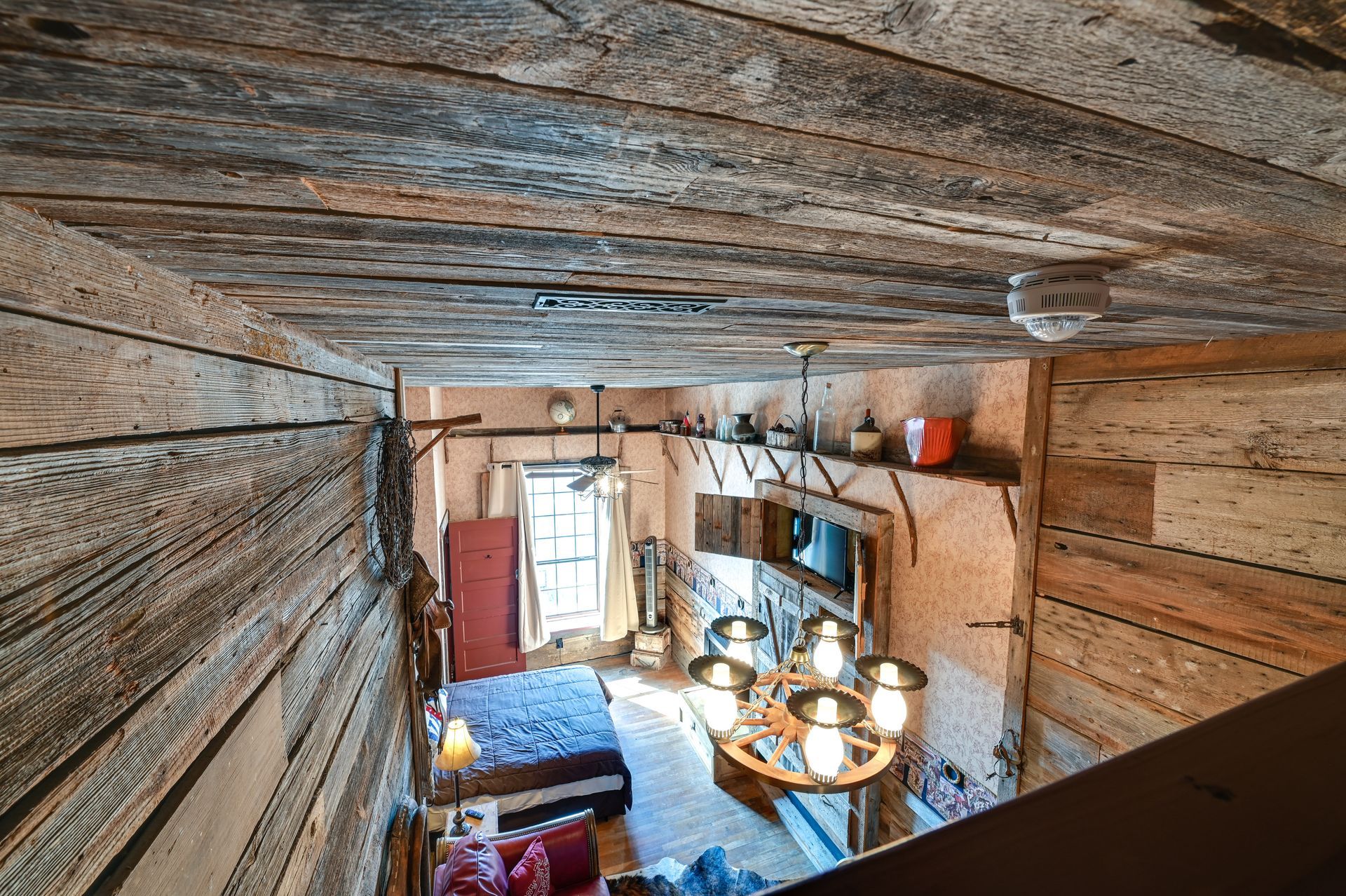 Un interior rústico de madera con una cama, una araña y una ventana.