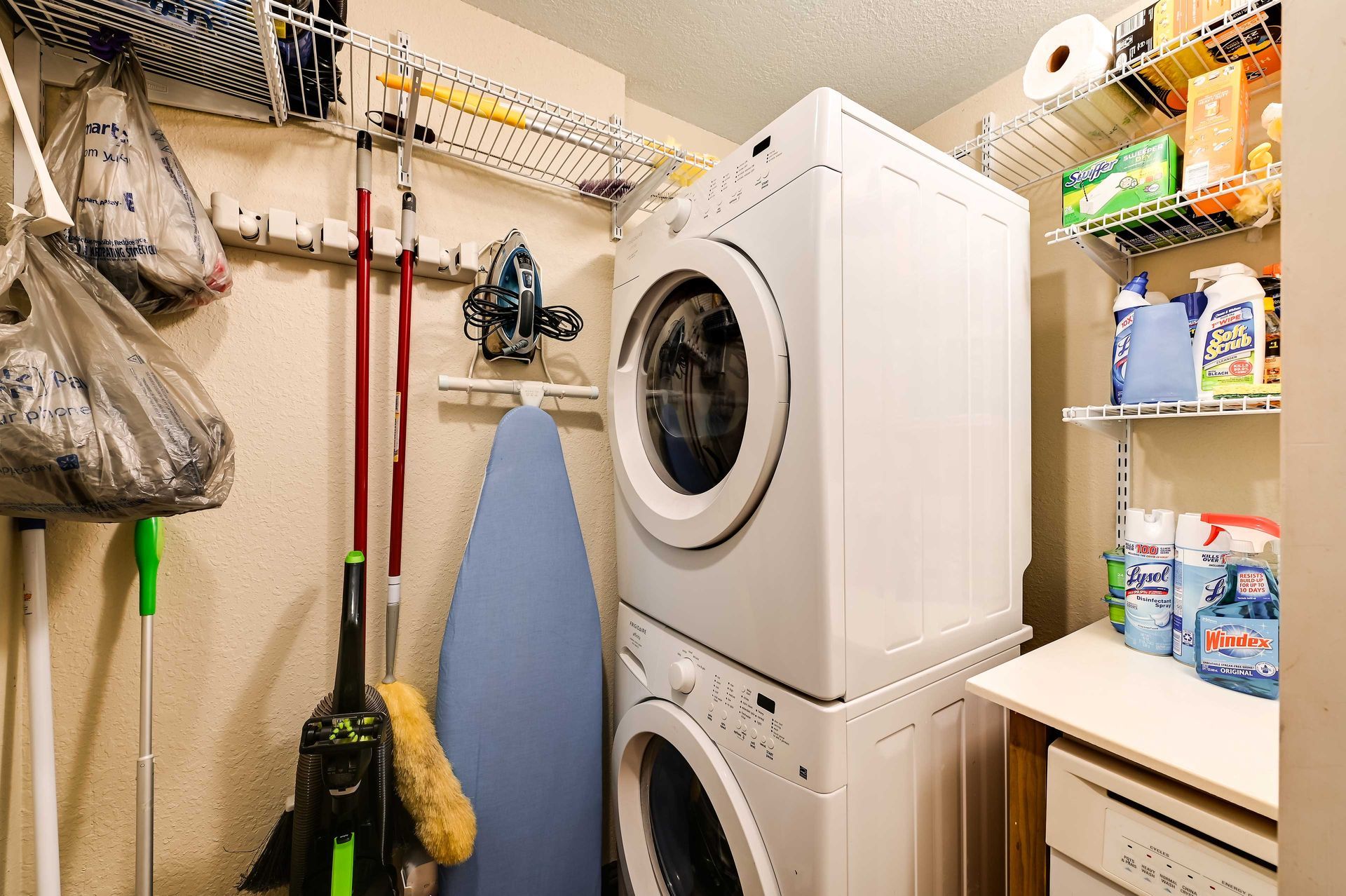 A laundry room with a washing machine, ironing board, and various cleaning supplies.