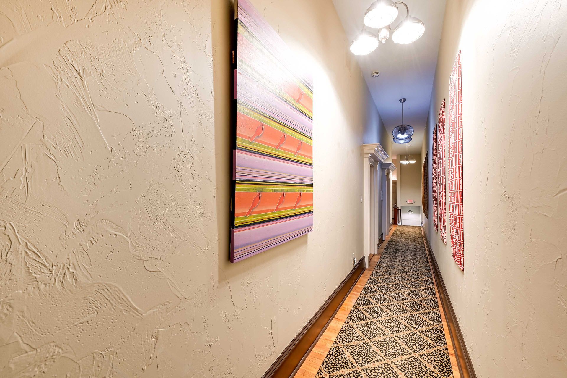 A hallway with textured walls, a patterned carpet, and artwork.