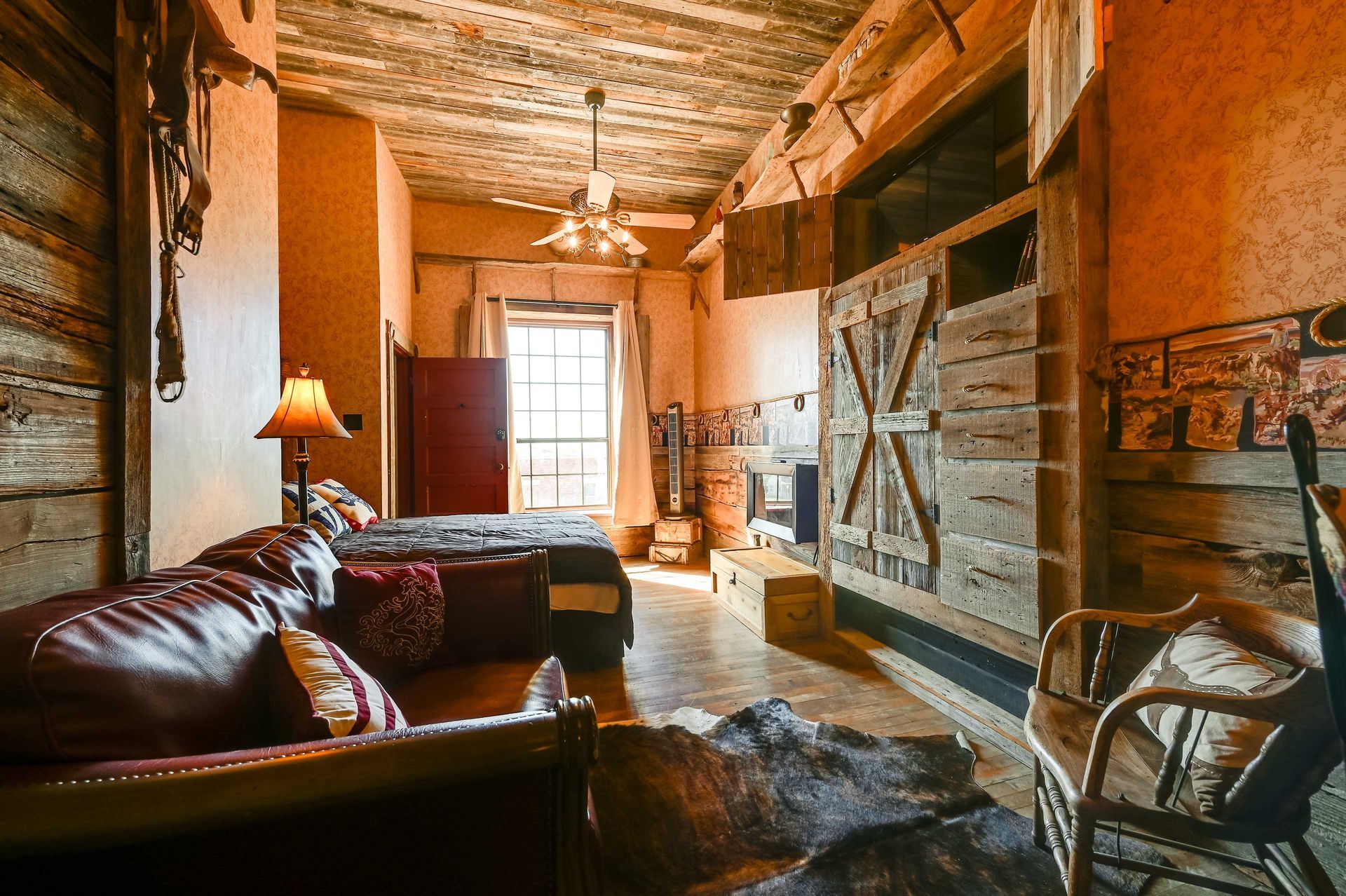 A rustic room with a bed, a wooden chair, a lamp, and a large wooden door.