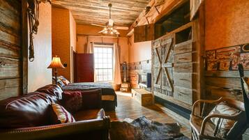 A rustic room with a bed, a wooden chair, a lamp, and a large wooden door.