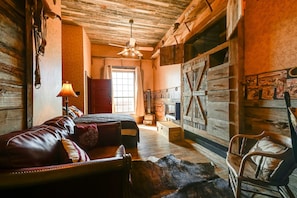 A rustic room with a bed, a wooden chair, a lamp, and a large wooden door.