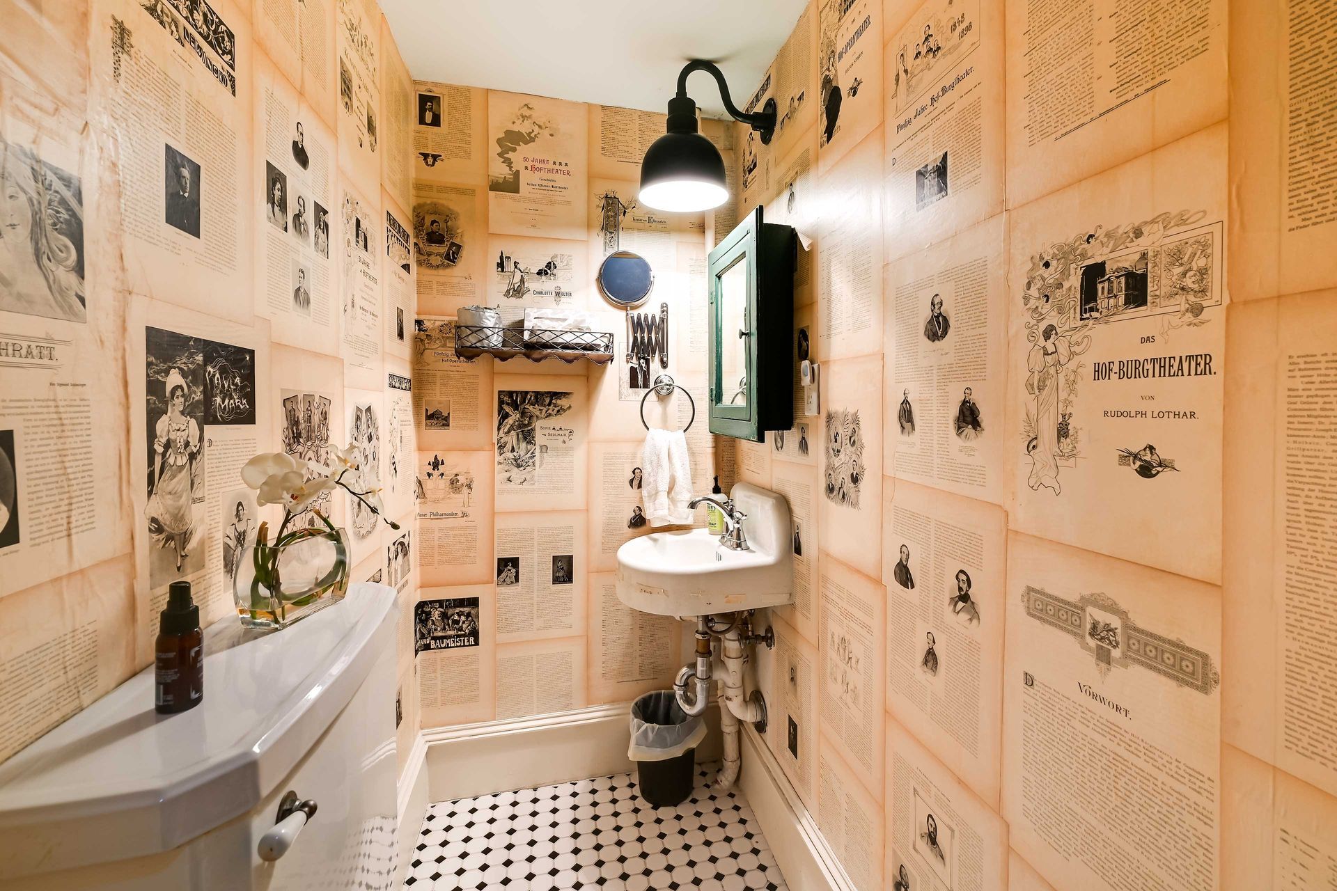 A bathroom with vintage newspaper wallpaper, a white sink, and a black floor lamp.
