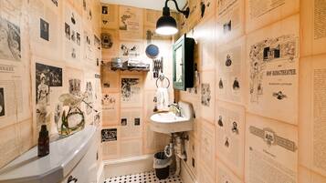 A bathroom with vintage newspaper wallpaper, a white sink, and a black floor lamp.
