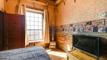 A room with a wooden floor, a bed, a fireplace, a window, and a wall with a decorative tile border.
