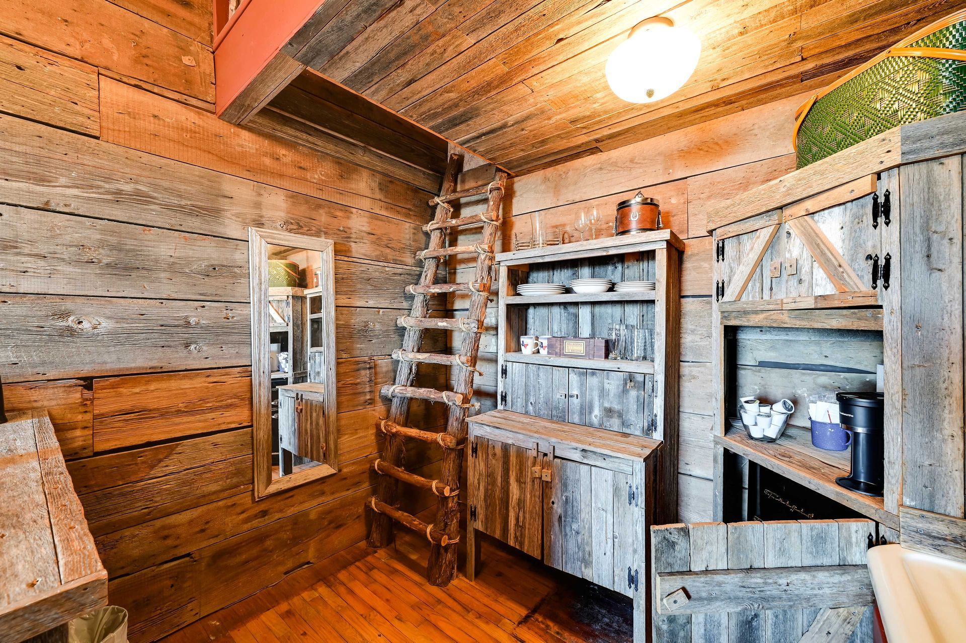 A rustic wooden interior with a ladder, shelves with dishes, and a mirror.