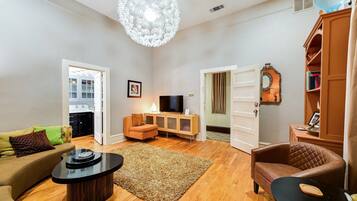 A spacious living room with a modern chandelier, a television, and a dining area with a table and chairs.