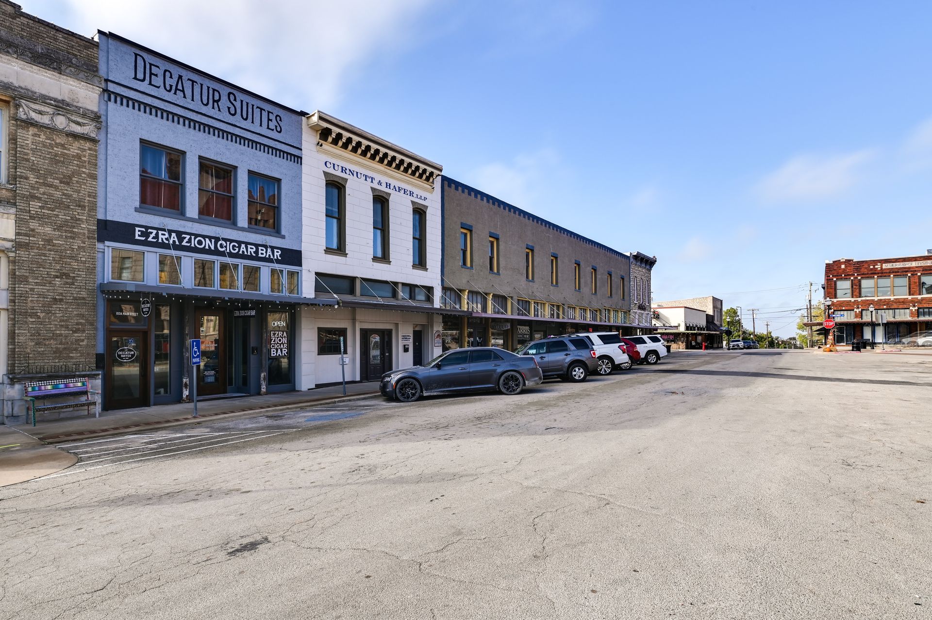A street with buildings including a bar named 'EZRA ZION CIGAR BAR' and a hotel named 'DECATUR SUITES'.