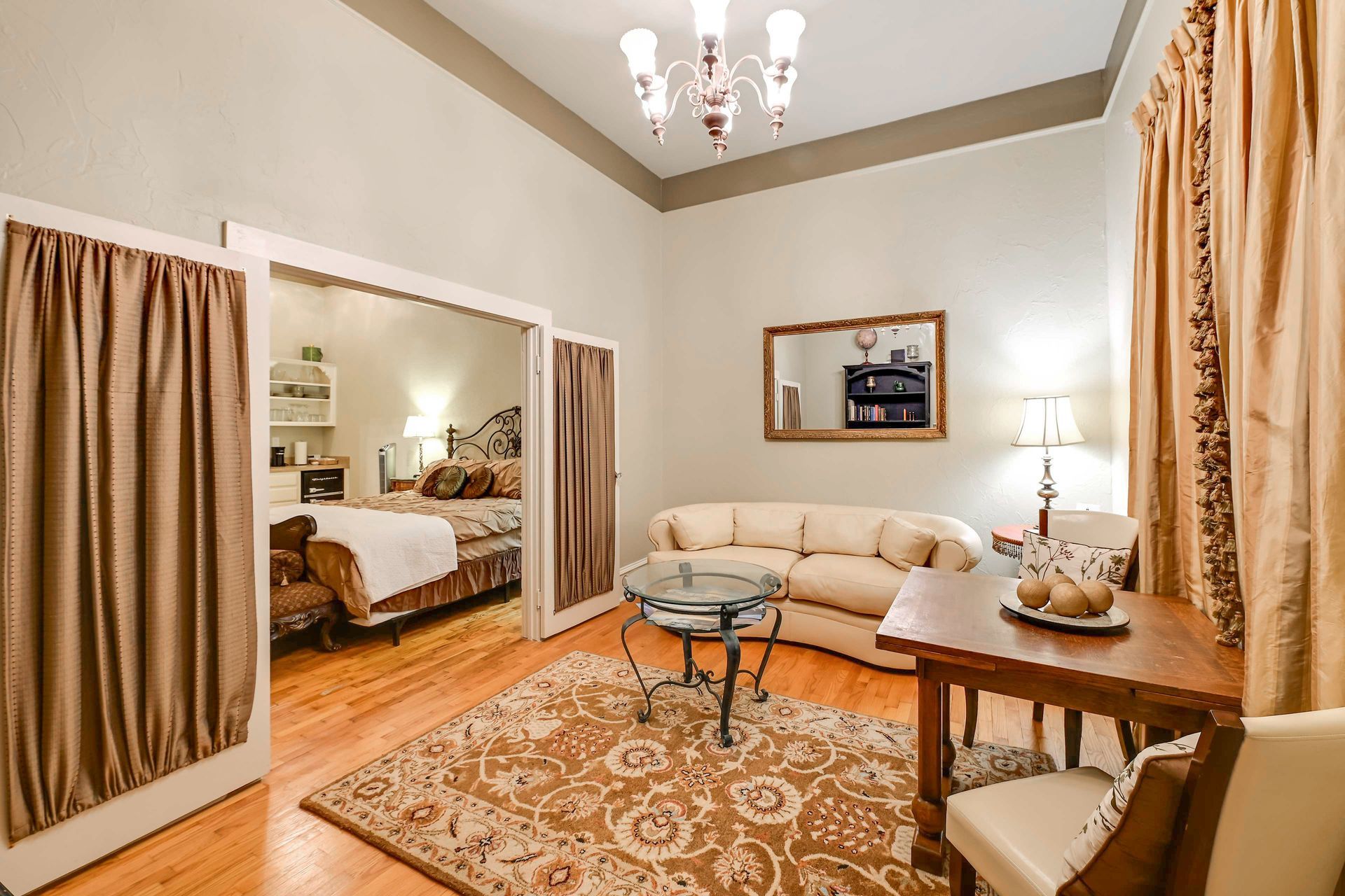 A living room with a sofa, a glass coffee table, a dining table, and a chandelier.