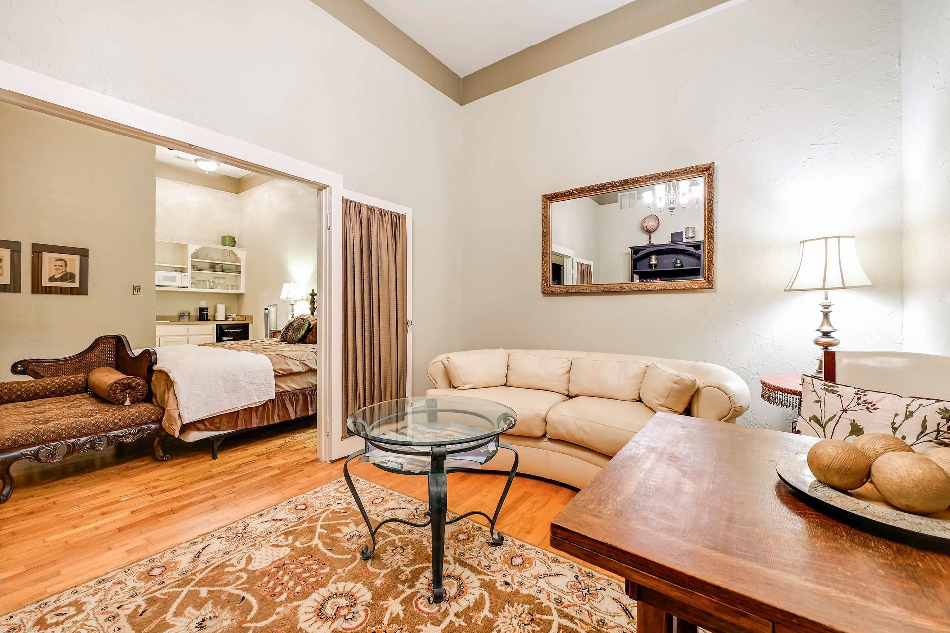 A living room with a sofa, a glass coffee table, a wooden side table, and a mirror on the wall.