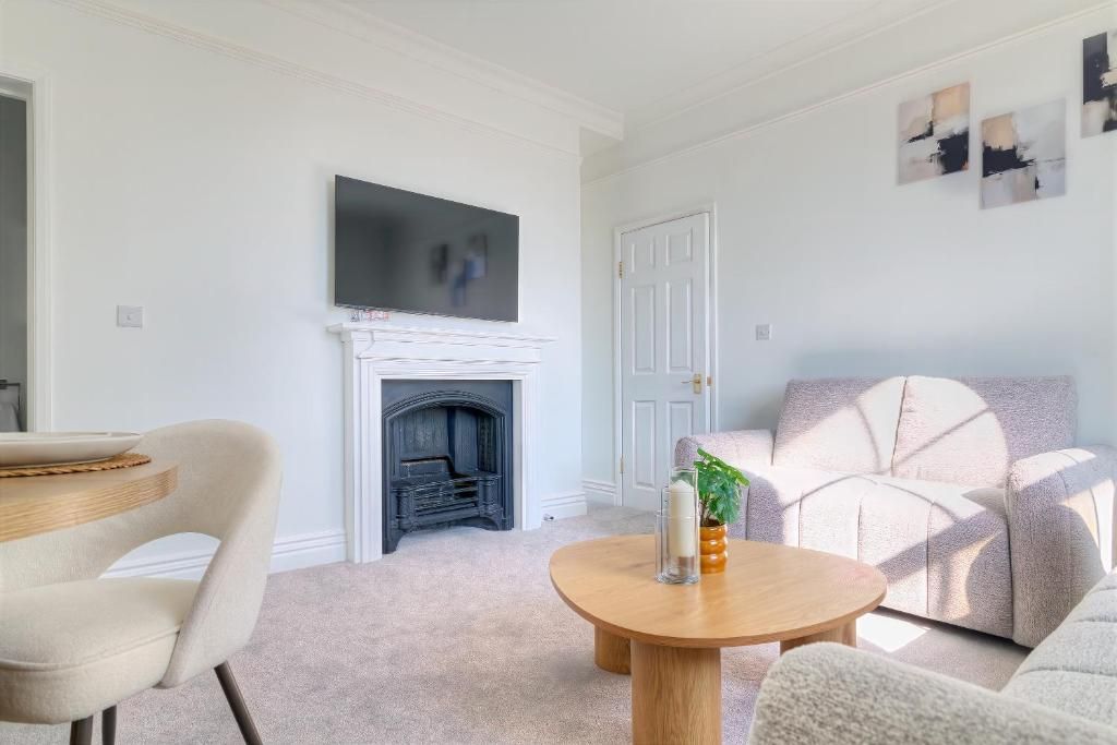 A living room with a fireplace, a television mounted above it, a round coffee table with candles, and a sofa.