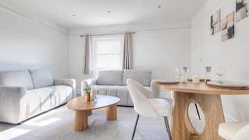 A modern living room with a sofa, a coffee table, and a dining table set for two.