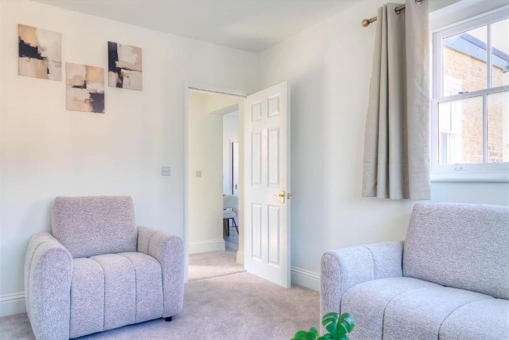A room with two grey armchairs, a white door, and a window with curtains.