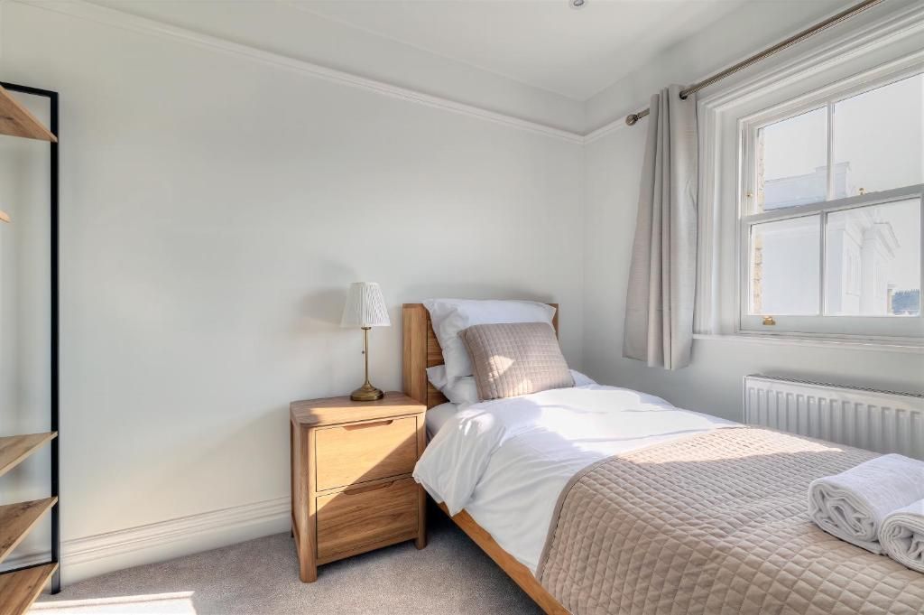 A bedroom with a bed, bedside table, lamp, and a window.