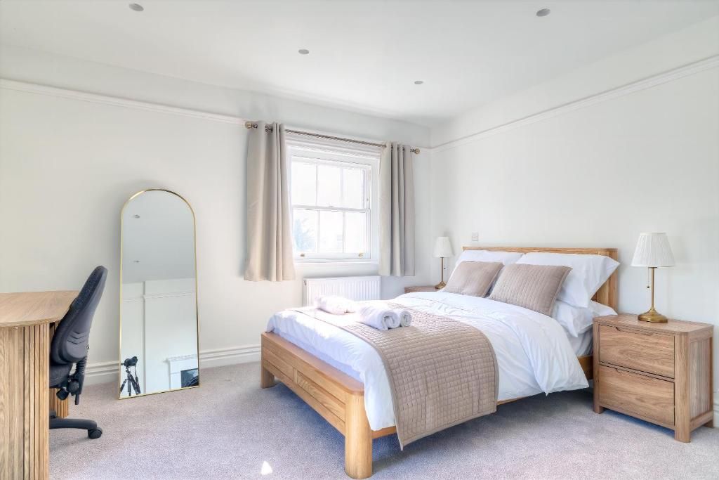 A bedroom with a bed, bedside tables, a desk, a chair, a mirror, and a window with curtains.