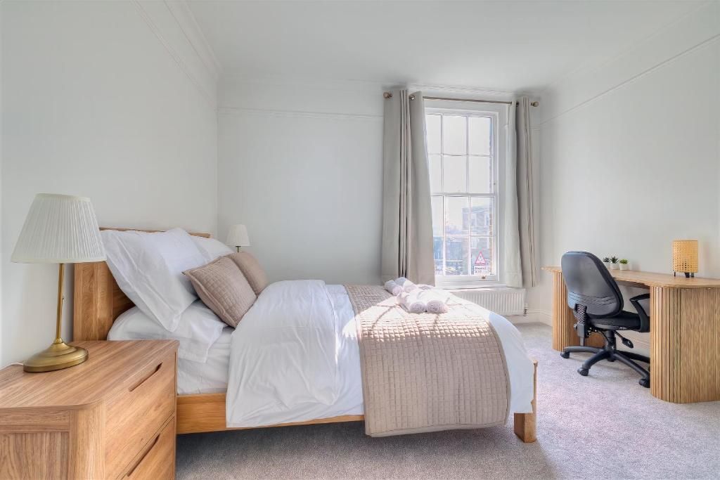 A bedroom with a bed, bedside table, lamp, desk, chair, and a window with curtains.