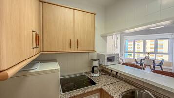 A compact kitchen with wooden cabinets, a built-in stove, a microwave, and a coffee maker.