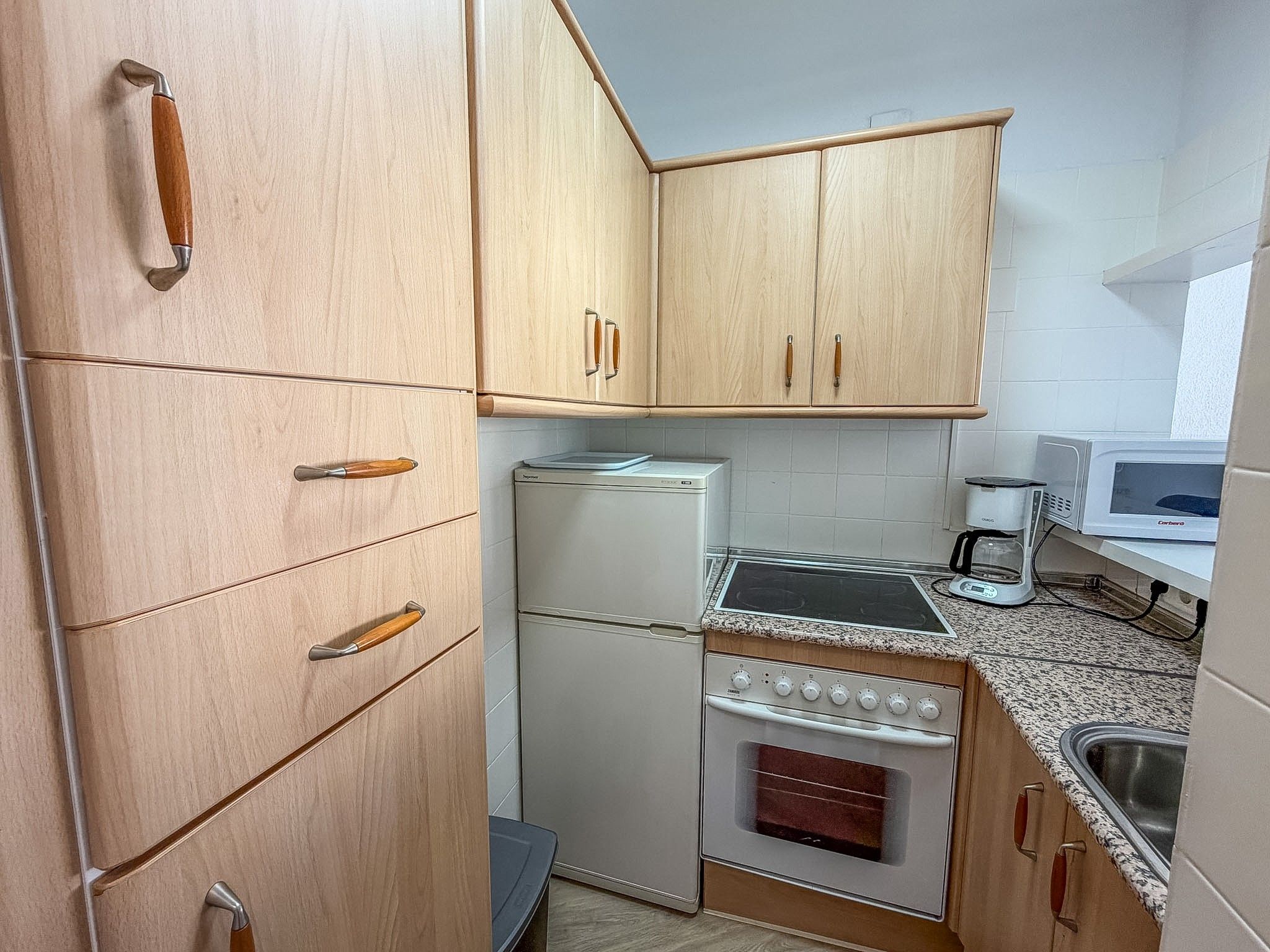 Une cuisine de taille réduite, dotée de meubles en bois, d’un réfrigérateur, d’une cuisinière et d’un four à micro-ondes.