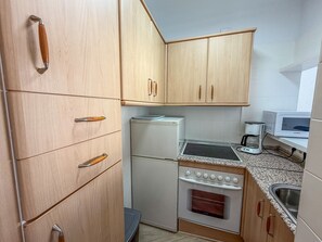 A compact kitchen with wooden cabinets, a refrigerator, a stove, and a microwave. - Apartment 'Apartamento en primera línea con vistas al mar en Torrox Costa' (Torrox)