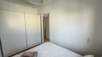 Une chambre à coucher comprenant un lit, une armoire, une porte donnant sur une autre pièce et un luminaire au plafond.