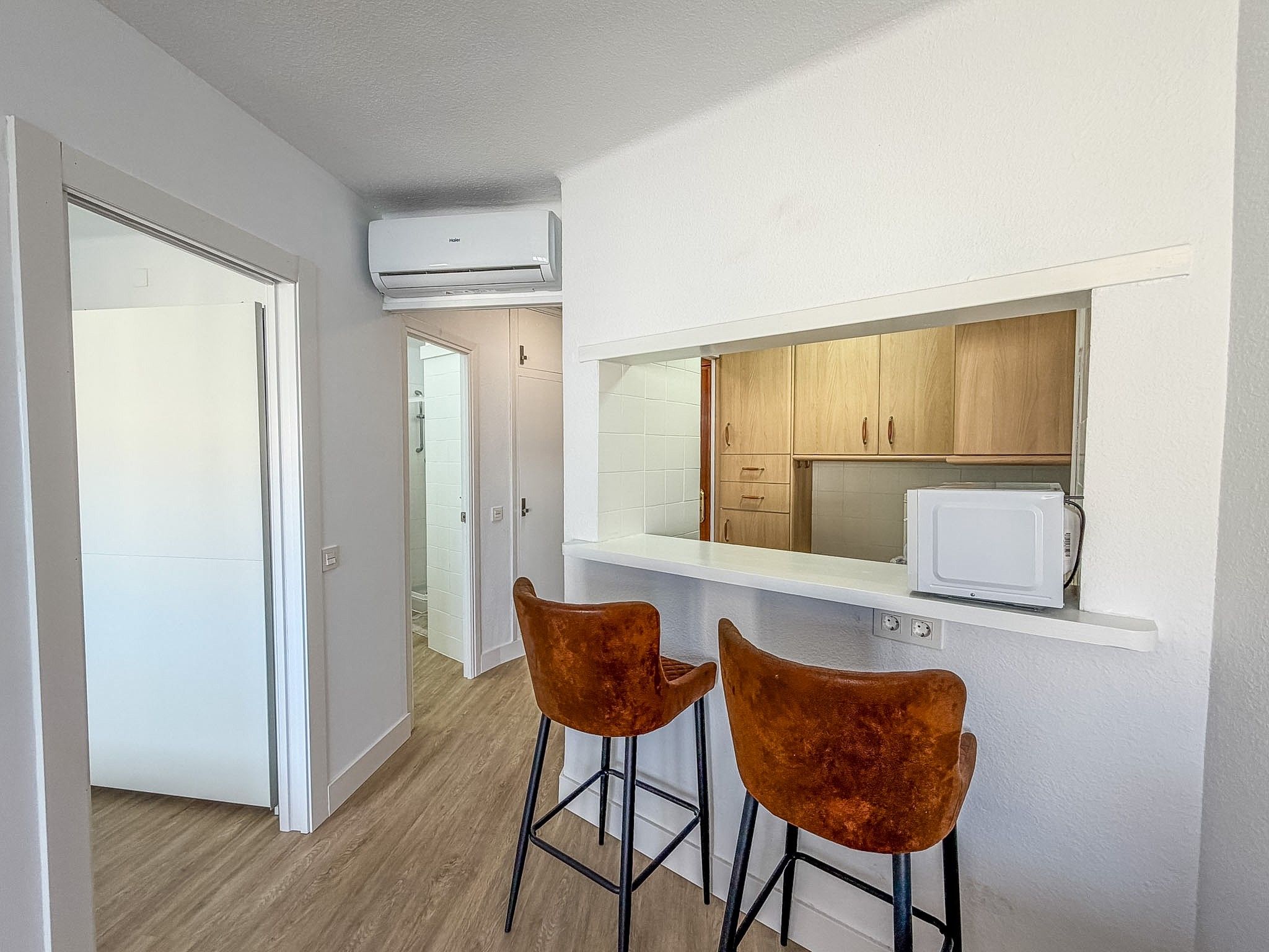 A compact kitchen with a microwave, wooden cabinets, and two bar stools.