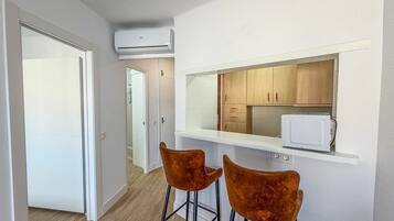A compact kitchen with a microwave, wooden cabinets, and two bar stools.