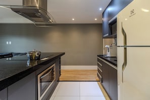 A modern kitchen with a black countertop, stainless steel appliances, and a wooden floor. - Matoso by Bhomy (São Paulo)