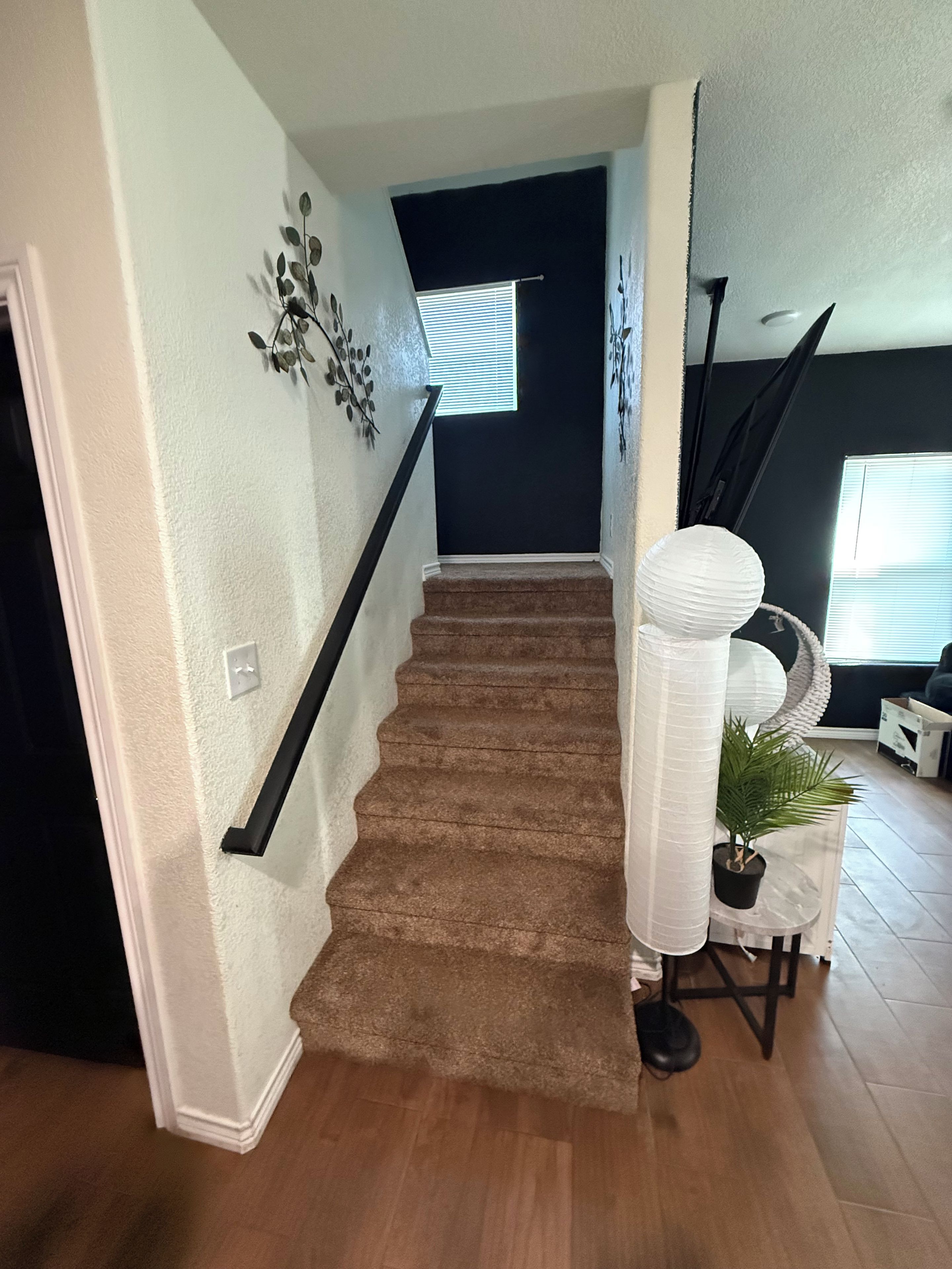 A staircase with a brown carpet, white walls, and a black railing.