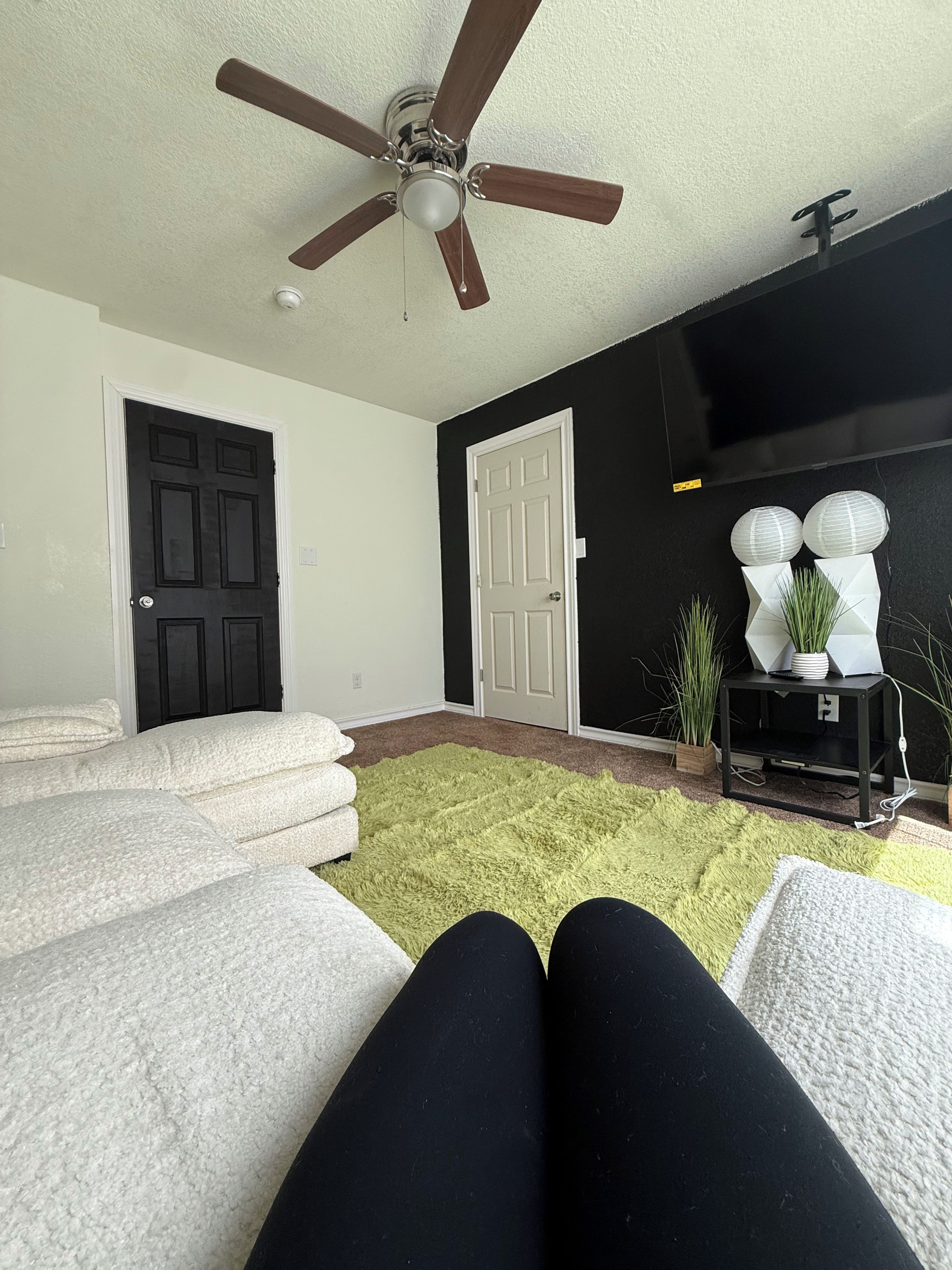 A living room with a ceiling fan, a black TV stand, and a green rug.