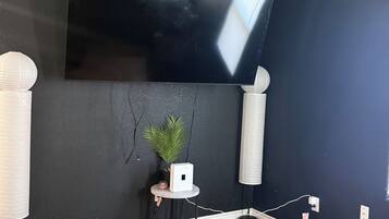 A room with a large flat-screen TV mounted on the wall, a small table with a plant, and a ceiling fan.