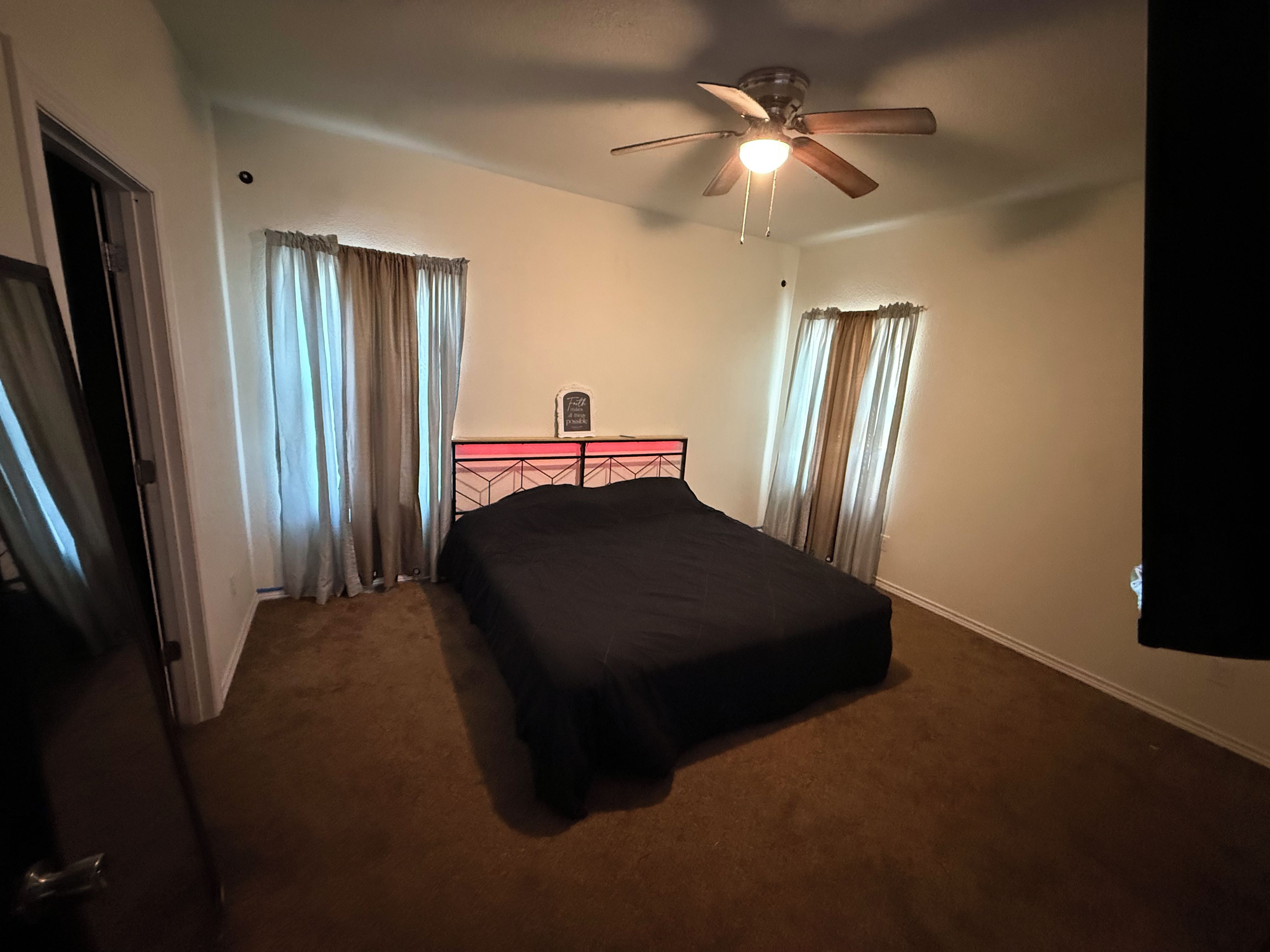 A bedroom with a single bed, a ceiling fan, and curtains on the windows.
