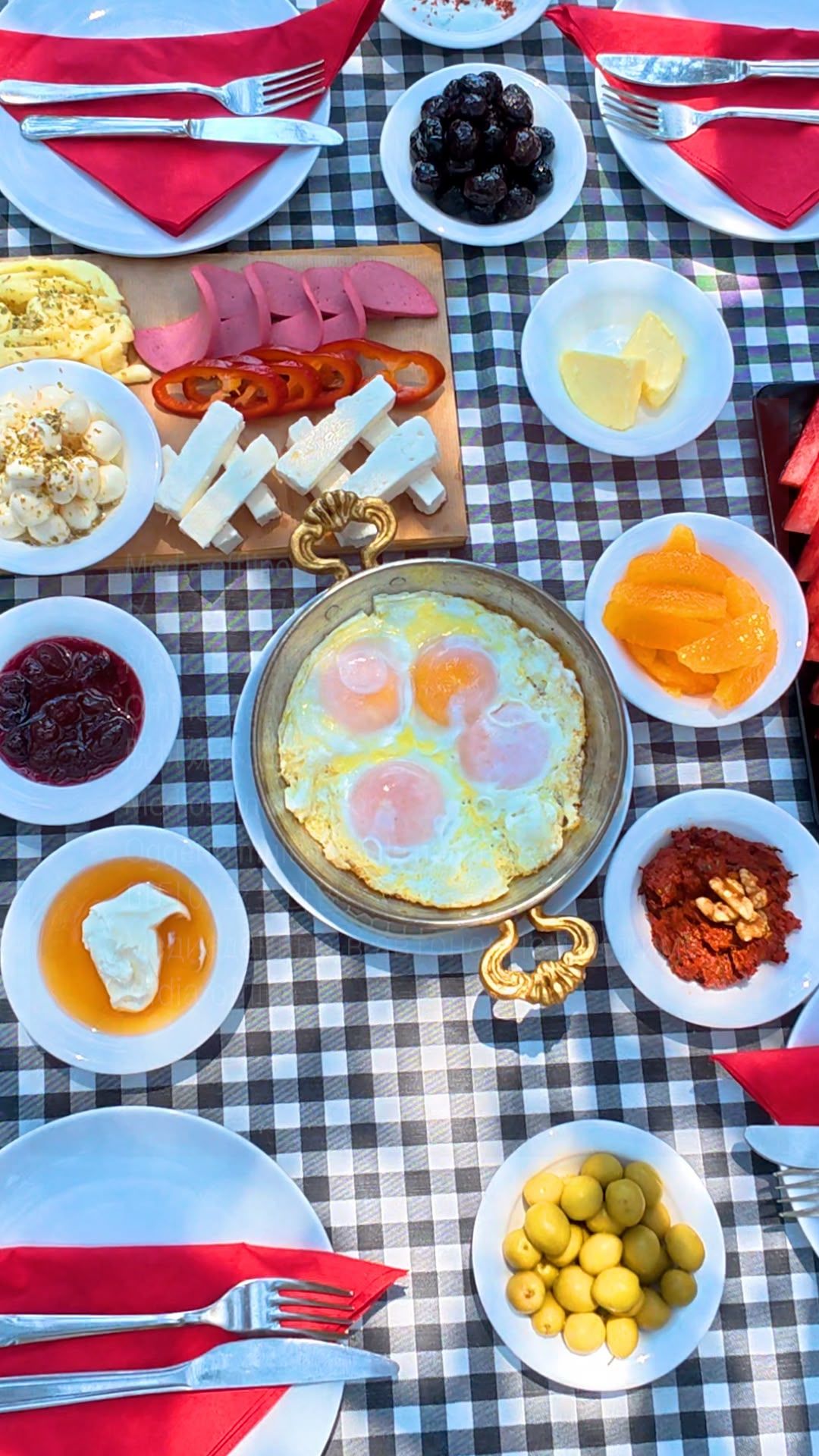 Una mesa con diversos platos, incluyendo huevos, queso y frutas, sobre un mantel a cuadros.