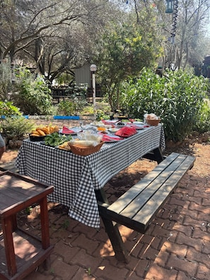 An outdoor picnic setup with a checkered tablecloth, a picnic bench, and various food items. - Alpstar Camping & Restaurant (Geyikbayiri)