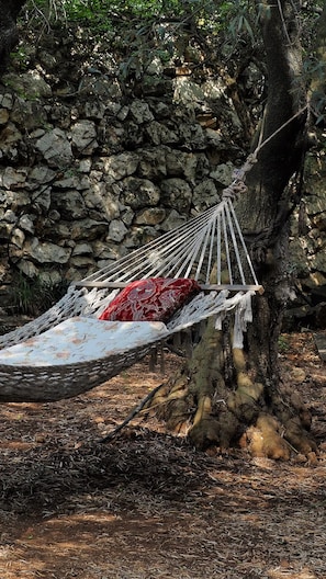 A hammock tied between trees in a natural setting with a stone wall in the background. - Alpstar Camping & Restaurant (Geyikbayiri)