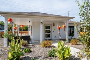 A modern house with a covered porch, a front door, and a small garden area with plants and a patio table. - South Campus Modern - Upscale & Walkable To Uo, Park & Shops 3 Bedroom Home (Eugene)