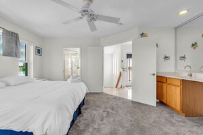 Ein Hotelzimmer mit Bett, Deckenventilator, Badezimmer mit Waschbecken und Spiegel sowie Blick ins Freie.