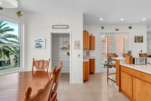 Eine moderne Küche mit Holzausstattung, ein Essbereich mit Holztisch und -stühlen und Blick auf eine Palme draußen.