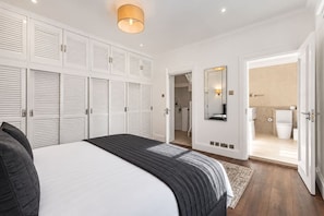 A bedroom with a bed, a wardrobe, a mirror, and a bathroom visible through an open door. - South Kensington 3-bed Mews Near Hyde Park (London)