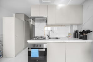 Una cocina moderna con armarios blancos, estufa de acero inoxidable, horno empotrado y un lavamanos con grifo amarillo.